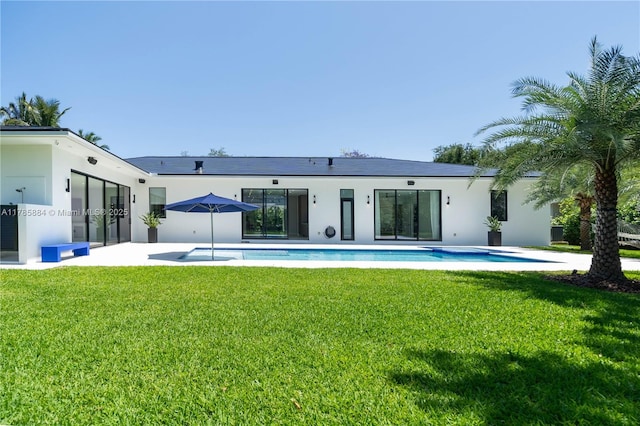 rear view of property featuring a yard, an outdoor pool, and stucco siding
