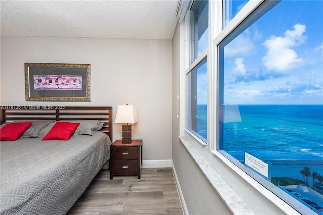 bedroom with a textured ceiling, a water view, wood finished floors, and baseboards