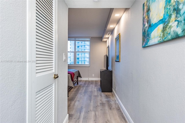 hallway featuring wood finished floors, a textured wall, and baseboards