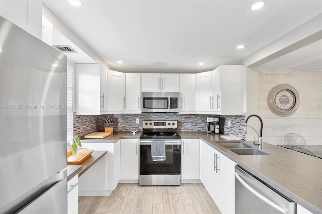 kitchen with stainless steel appliances, visible vents, a sink, tasteful backsplash, and white cabinetry