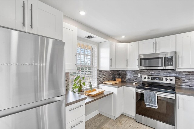 kitchen with white cabinets, stainless steel appliances, visible vents, and decorative backsplash