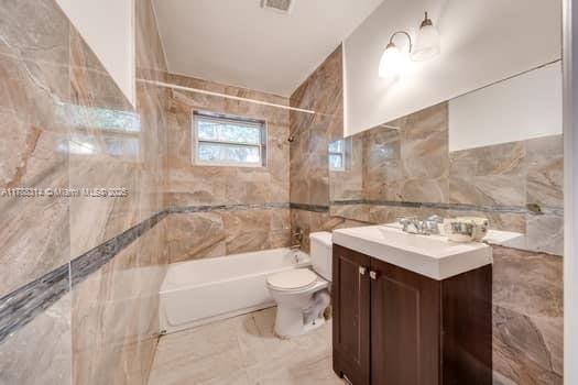 bathroom with vanity, toilet, tile walls, visible vents, and washtub / shower combination
