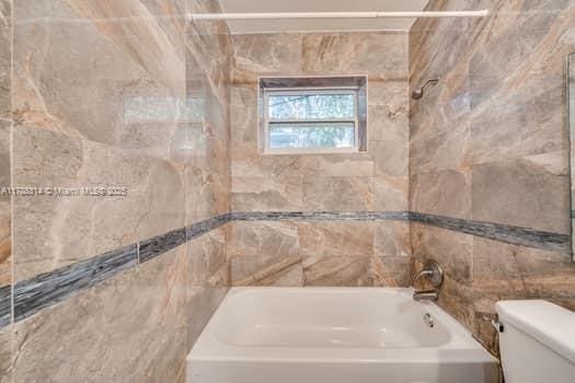bathroom with tile walls, shower / washtub combination, and toilet