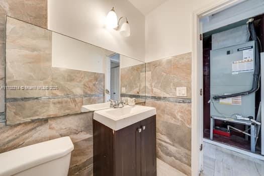 half bathroom featuring tile walls, vanity, and toilet