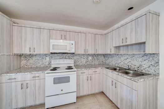 kitchen featuring light stone countertops, decorative backsplash, white appliances, and a sink