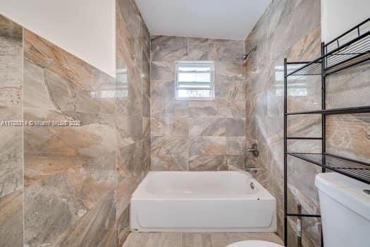 bathroom featuring tile walls, toilet, and shower / washtub combination