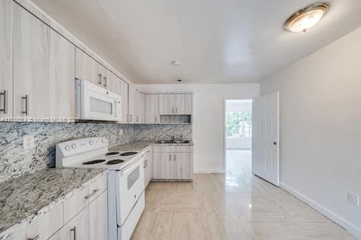 kitchen with light stone countertops, baseboards, white appliances, and tasteful backsplash