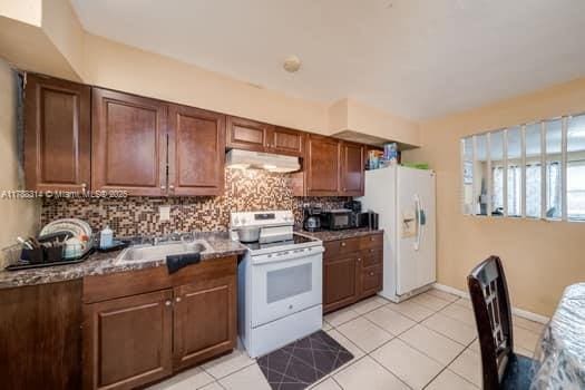 kitchen featuring a sink, tasteful backsplash, white appliances, under cabinet range hood, and light tile patterned floors