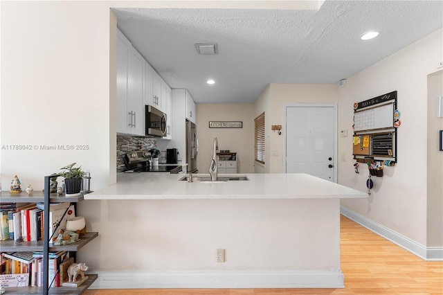 kitchen featuring appliances with stainless steel finishes, a peninsula, tasteful backsplash, a sink, and light countertops