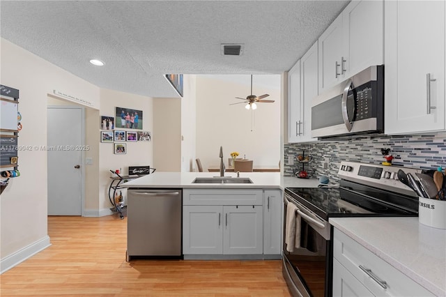 kitchen with stainless steel appliances, a sink, a peninsula, light countertops, and tasteful backsplash