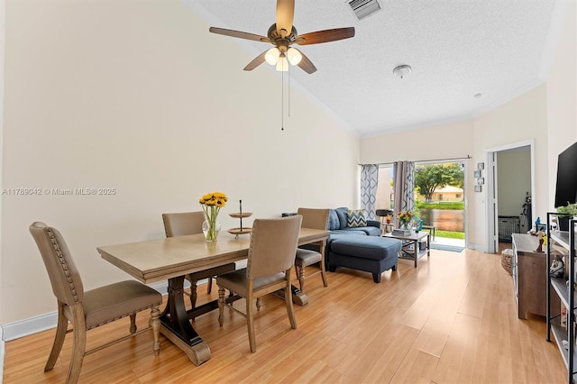 dining area featuring a ceiling fan, light wood finished floors, a textured ceiling, crown molding, and high vaulted ceiling