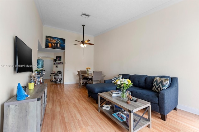 living area with light wood-type flooring, ceiling fan, ornamental molding, and baseboards