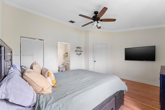 bedroom featuring light wood finished floors, ornamental molding, baseboards, ensuite bath, and a ceiling fan