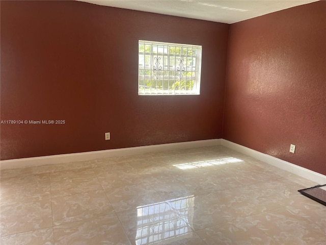 unfurnished room with a textured wall, tile patterned floors, and baseboards