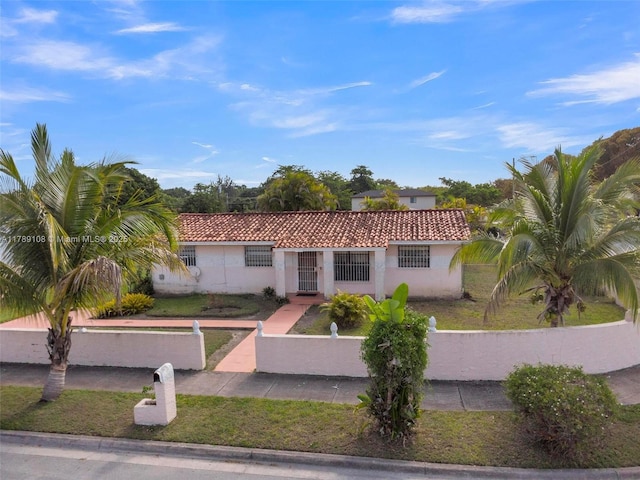 mediterranean / spanish home with stucco siding, a tile roof, and a fenced front yard