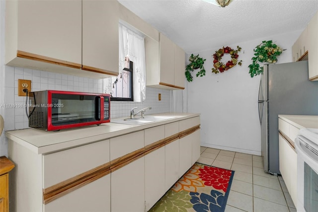kitchen with a sink, decorative backsplash, light tile patterned floors, light countertops, and white electric stove