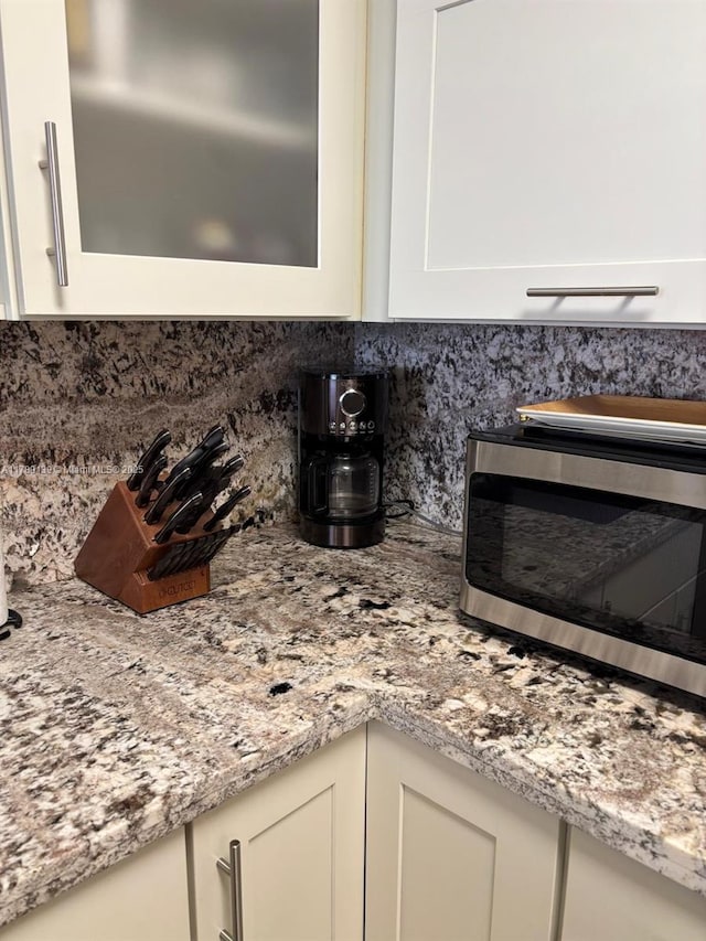 500 Three Islands Blvd Unit 313, Hallandale Beach, FL 33009 - kitchen view of stainless steel microwave, tasteful backsplash, white cabinetry, light stone counters, and glass insert cabinets