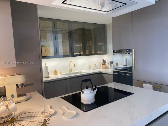 1450 Brickell Bay Dr Unit 1709, Miami, FL 33131 - kitchen with a sink, glass insert cabinets, modern cabinets, black electric cooktop, and gray cabinetry