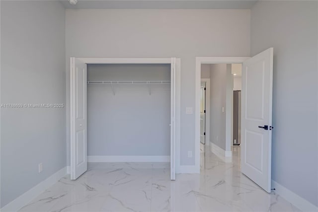 unfurnished bedroom with refrigerator, marble finish floor, baseboards, and a closet