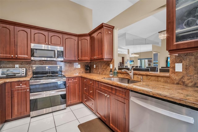 kitchen with a sink, light tile patterned floors, a toaster, appliances with stainless steel finishes, and light stone countertops