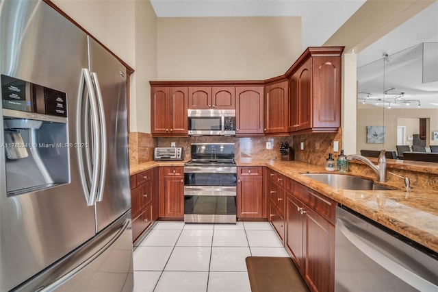 kitchen with tasteful backsplash, a sink, light tile patterned floors, stainless steel appliances, and light stone countertops