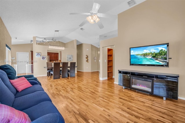 living area with a ceiling fan, wood finished floors, baseboards, lofted ceiling, and visible vents