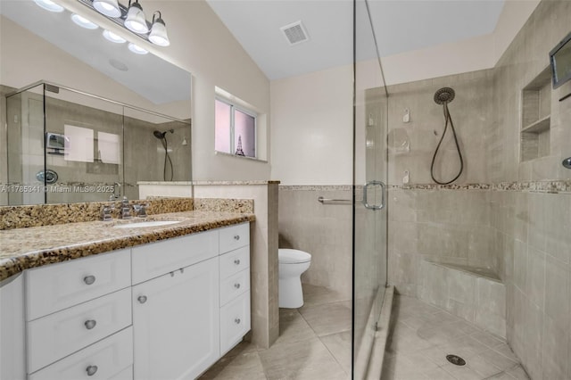 bathroom with a shower stall, visible vents, toilet, vanity, and tile walls