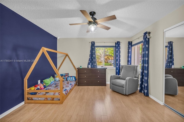 bedroom featuring baseboards, wood finished floors, a textured ceiling, and ceiling fan