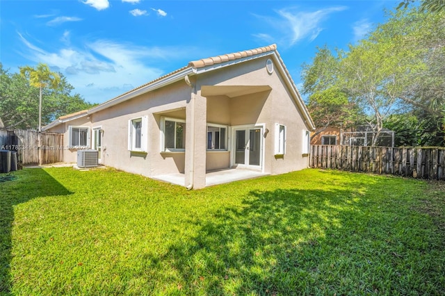 rear view of house with a fenced backyard, a yard, central AC, and stucco siding
