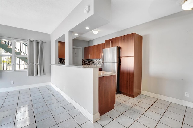 2200 S Ocean Dr Unit N116, Hollywood, FL 33019 - kitchen featuring light tile patterned flooring, brown cabinetry, freestanding refrigerator, baseboards, and decorative backsplash