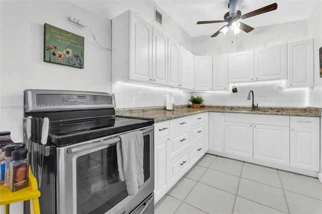 kitchen with dark stone countertops, a sink, stainless steel range with electric cooktop, light tile patterned floors, and ceiling fan