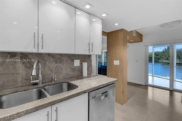 kitchen featuring stainless steel dishwasher, a sink, light tile patterned floors, white cabinets, and backsplash