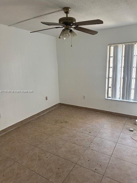 tiled empty room featuring a ceiling fan and a textured ceiling