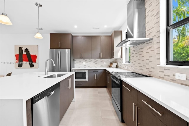 kitchen with a sink, a wealth of natural light, light countertops, wall chimney exhaust hood, and appliances with stainless steel finishes