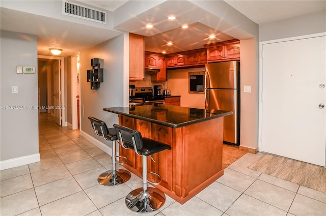 kitchen with under cabinet range hood, visible vents, light tile patterned floors, appliances with stainless steel finishes, and a breakfast bar area