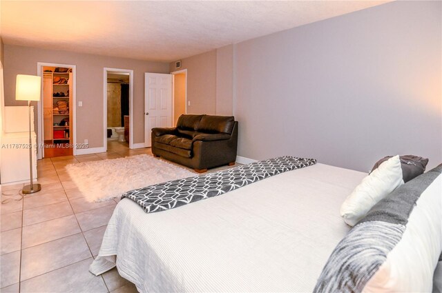 bedroom with tile patterned floors, ensuite bathroom, a walk in closet, baseboards, and visible vents