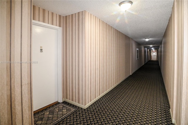 hallway featuring wallpapered walls, baseboards, and a textured ceiling