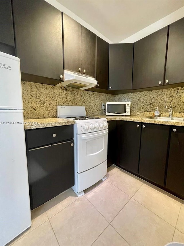kitchen featuring under cabinet range hood, a sink, light tile patterned flooring, white appliances, and tasteful backsplash