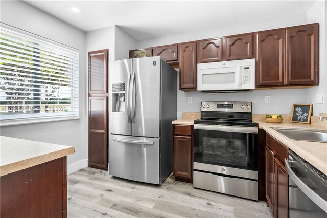 kitchen with light wood finished floors, stainless steel appliances, a sink, recessed lighting, and light countertops