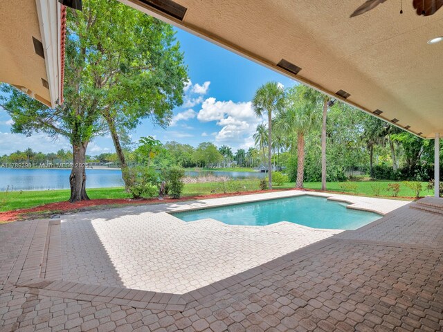 outdoor pool with a water view, a patio area, a ceiling fan, and a yard