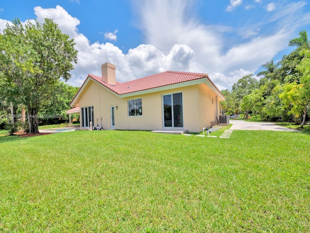 back of property featuring a tile roof, a chimney, central AC, and stucco siding