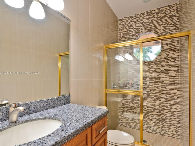 bathroom with a stall shower, toilet, vanity, and tile walls