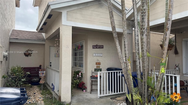12222 SW 148th St, Miami, FL 33186 - view of exterior entry with a porch, stucco siding, and roof with shingles