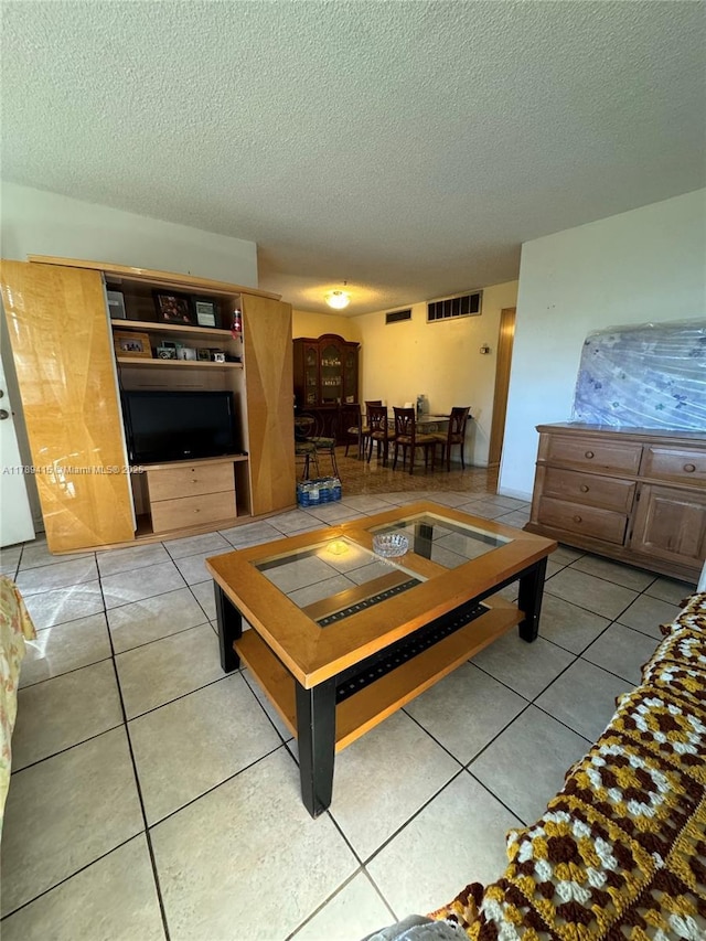 living room with a textured ceiling, visible vents, and light tile patterned floors