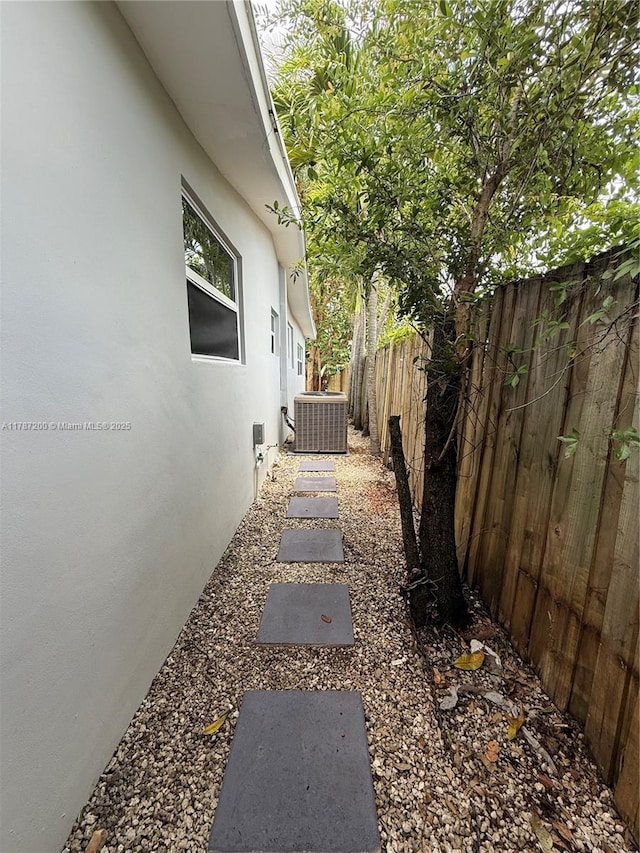 view of side of property with stucco siding, central AC unit, and fence
