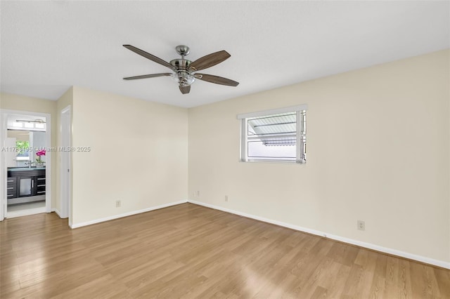 empty room with light wood-style floors, a ceiling fan, and baseboards