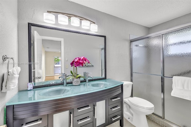 bathroom with a textured wall, a sink, a shower stall, and double vanity