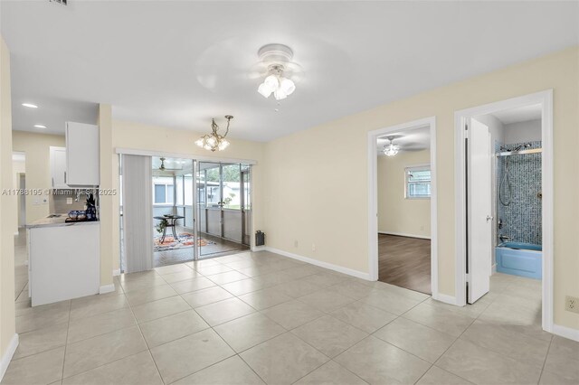 unfurnished dining area featuring recessed lighting, baseboards, light tile patterned floors, and ceiling fan with notable chandelier