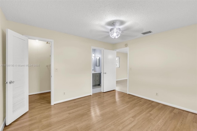 unfurnished bedroom featuring light wood finished floors, visible vents, a walk in closet, baseboards, and a textured ceiling