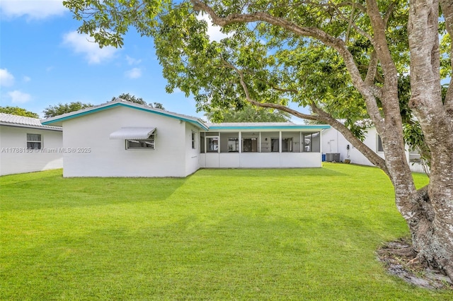 back of house featuring a yard, central air condition unit, a sunroom, and stucco siding